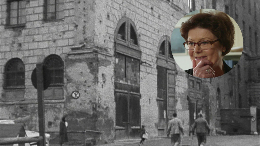 Filmstill aus "Mit den Füßen fängt es an – Ein Tag beim Ballett der Bayerischen Staatsoper". Das Münchner Nationaltheater 1955 mit Bombenschäden. Eingeblendet ist Corinna Schott, ehemalige Ballettschülerin