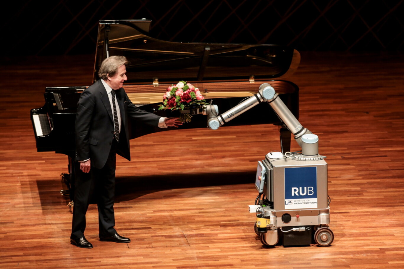 Rudolf Buchbinder empfängt Blumen von einem Roboter